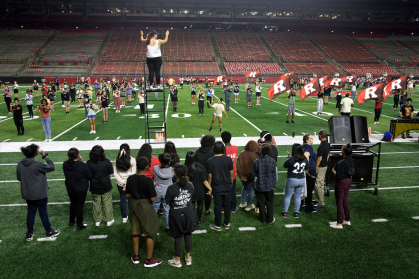 Drum major Zoe D'Amico (MGSA senior music major) stands on a ladder leading the rehearsal with NBHS students looking on