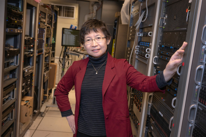 Rutgers computer Scientist Jie Gao standing in front of large computers