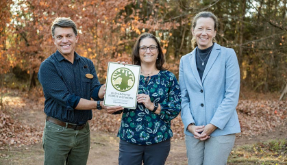 Three .people stand together outside in a wooded area