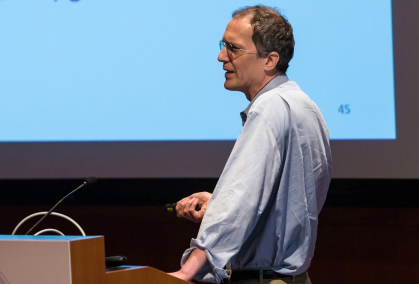 Man standing sideways lecturing before a screen.