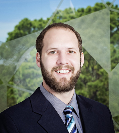 man in black jacket, grey shirt and striped tie with trees in background