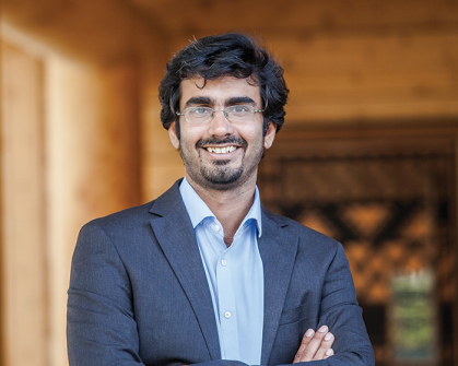 Man standing in a paneled room and wearing a blue suit jacket and blue shirt.