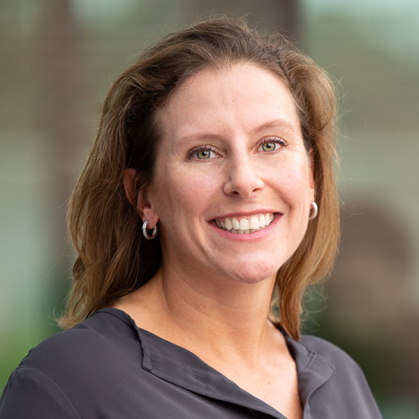 woman in gray shirt standing in front of an off-white background.