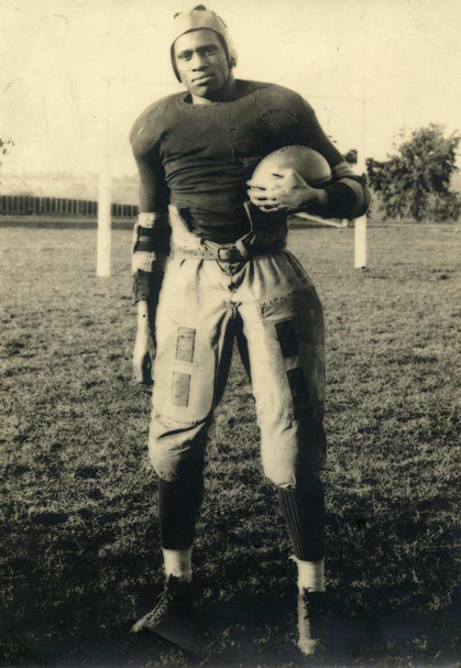 Paul Robeson poses in uniform holding a football.