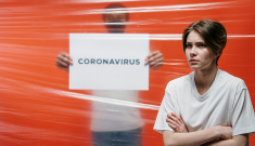 Women standing infront of orange background and a sign that says Coronavirus