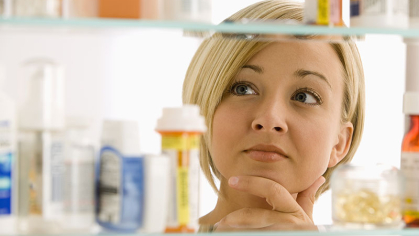 Woman behind a medicine cabinet with hand on chin, pondering selection of medicines